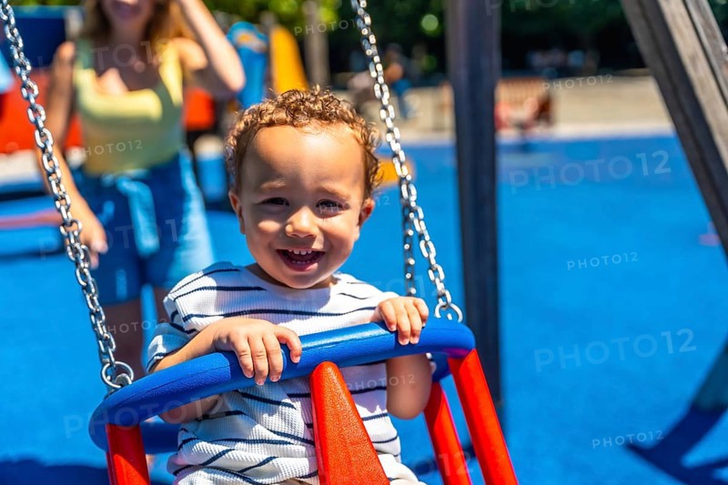 Happy toddler smiles while enjoying a swing ride at the playground, creating a joyful childhood scene