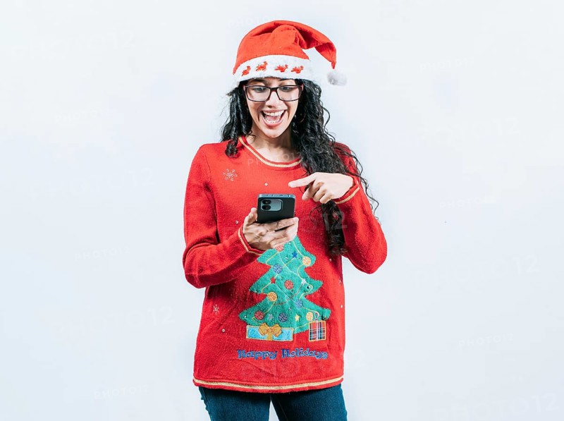 Happy girl in Christmas sweater looking pointing phone screen, isolated