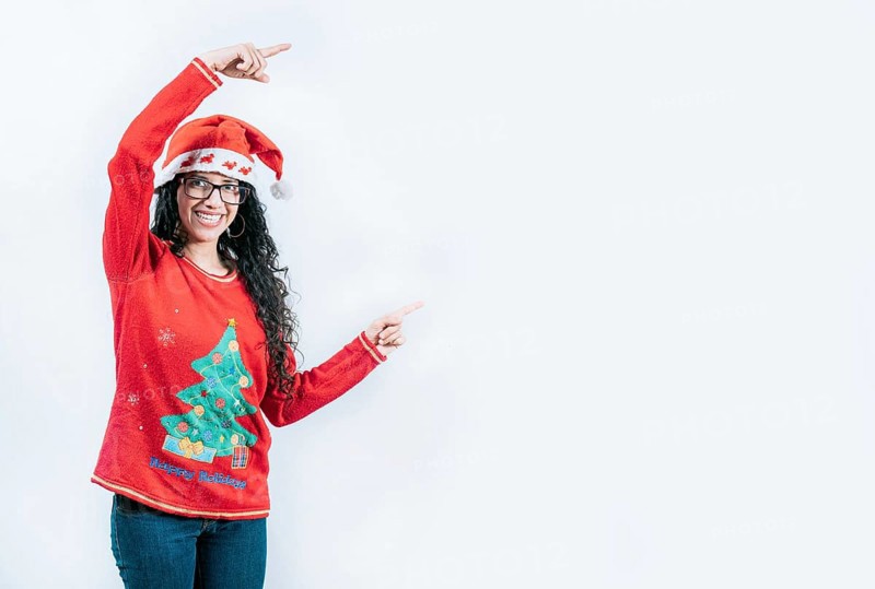 Smiling girl in Christmas sweater pointing to the side, isolated. Happy young woman in Christmas sweater recommending and pointing aside