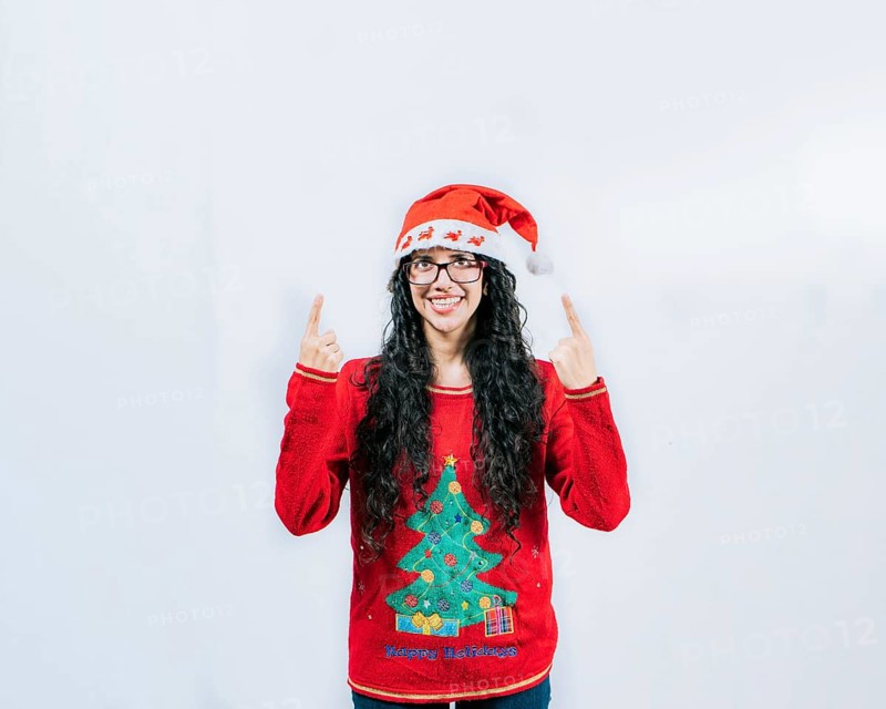 Smiling girl in Christmas hat pointing up isolated. Beautiful girl in Christmas sweater showing and pointing up