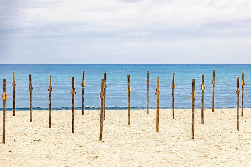 Sandy beach by the Mediterranean Sea with wooden poles for parasols and a seascape view to the horizon, Mallorca, Spain