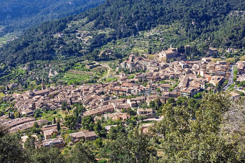 High angle view at a mountain village on a slope with lush green foliage a sunny summer day, Valldemossa, Mallorca, Spain