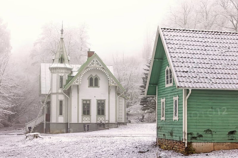 Old idyllic white wooden house with carpentry and a green garden shed on a cold winter day with snow and frost, Falköping, Sweden