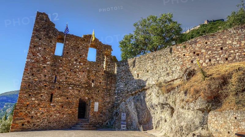 Lower main entrance, Historic ruins with flags in front of stony terrain under blue sky, Mystras, Mistra, UNESCO World Heritage Site, Medieval Byzantine ruined city, northwest of Sparta, foothills of the Taygetos Mountains, Peloponnese, peninsula, Greece