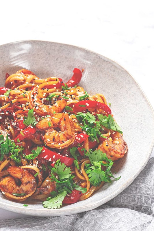 Udon noodles, shrimp with vegetables and fresh herbs, in a bowl with chopsticks, light background, homemade, no people