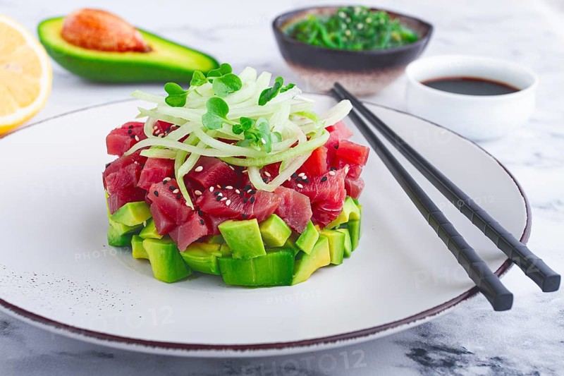 Fresh tuna tartare with avocado served on a marble table with soy sauce and seaweed salad