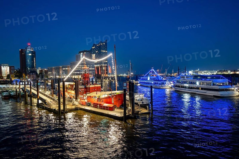 View of illuminated ships on the Elbe promenade with restaurant Das Feuerschiff LV 13, City Sporthafen, behind Speicherstadt with Elbphilharmonie and Columbus Haus, blue hour, Hamburg, Germany