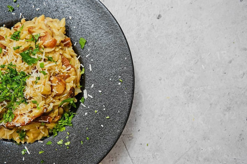 A delicious plate of risoni pasta combined with porcini mushrooms is presented beautifully. The dish is garnished with fresh herbs and grated cheese, showcasing a delightful culinary creation