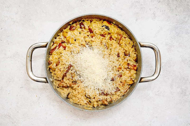 A delicious risoni dish with porcini mushrooms is presented in a pan. This comforting meal is topped with freshly grated parmesan cheese, showcasing a blend of flavors. Perfect for dinner enjoyment