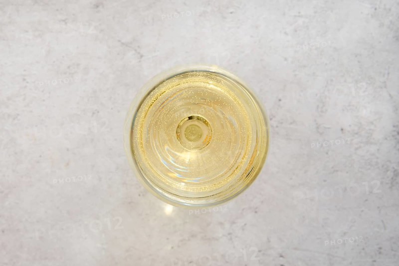 Close-up overhead view of a glass filled with white wine on a light textured surface