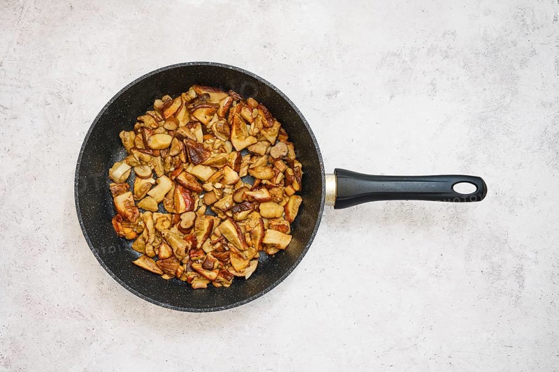 Diced porcini mushrooms are frying in a black pan, creating a savory meal. The cooking process showcases golden-brown pieces and a delicious aroma filling the kitchen