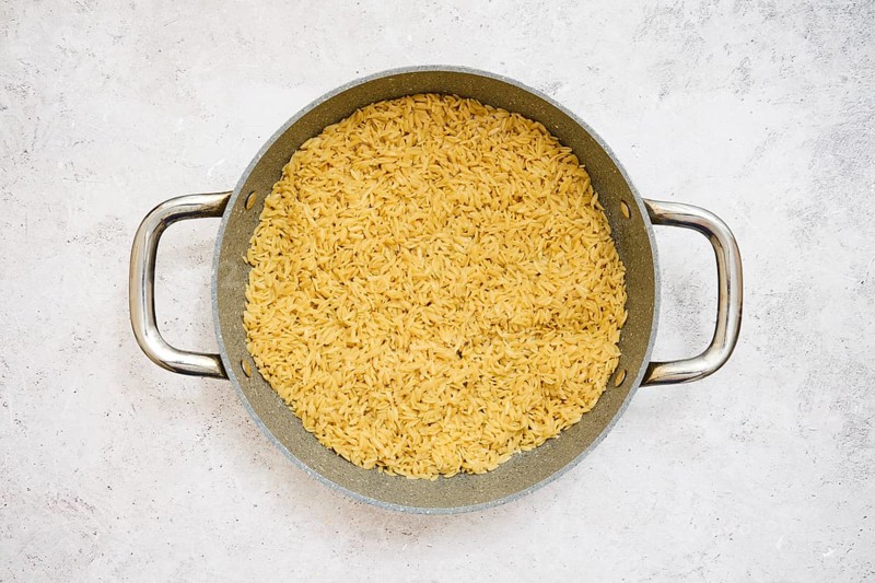 A pot filled with perfectly cooked risoni pasta on a neutral surface. This dish showcases a rich golden color, hinting at flavorful ingredients and a warm home cooking atmosphere