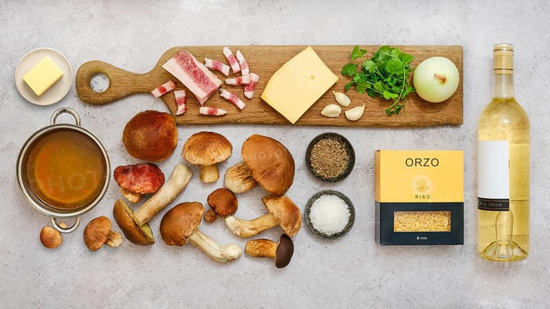 Fresh ingredients for a tasty risoni dish with porcini mushrooms are beautifully arranged on a countertop. This cozy kitchen scene showcases the vibrant colors and textures of each item