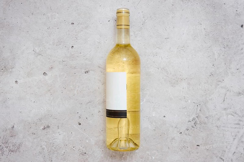 A white wine bottle with a blank label on a light grey textured surface. The setting suggests a calm moment for wine tasting or a casual gathering with friends