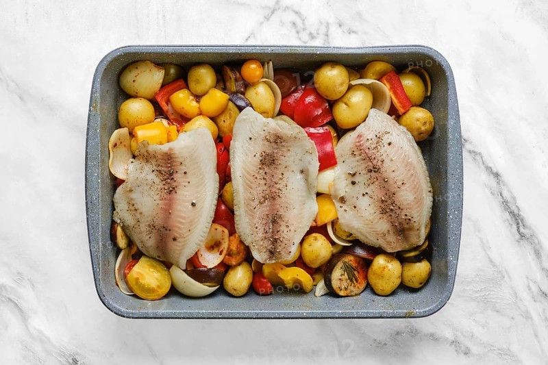 Fish fillets on a bed of colorful roasted vegetables, including onions, peppers, and baby potatoes