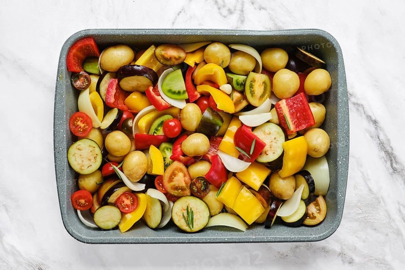 A vibrant mix of fresh vegetables is arranged in a baking tray, showcasing colorful peppers, potatoes, and tomatoes. This healthy preparation is ideal for roasting and enjoying a nutritious dish