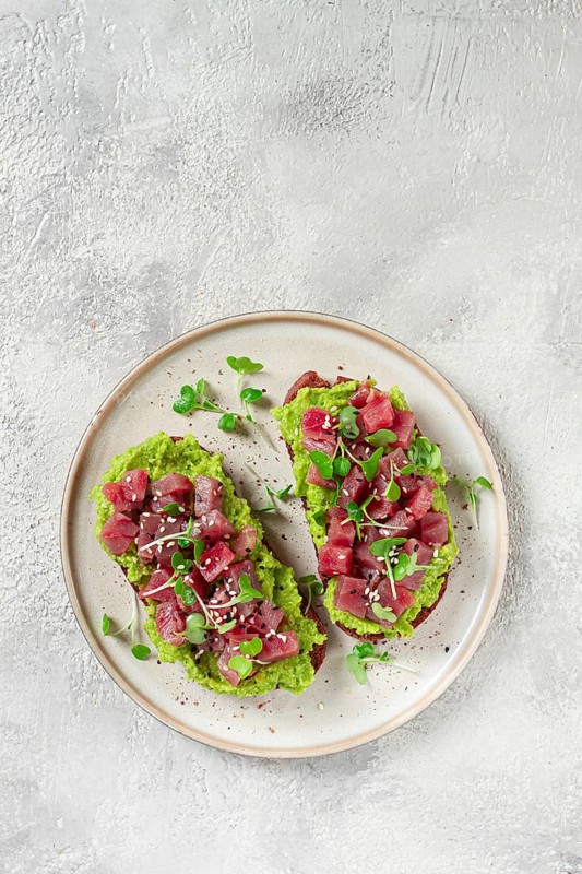 Toasts with fresh tuna and avocado, spread on black bread and sprinkled with microgreens, breakfast, healthy food