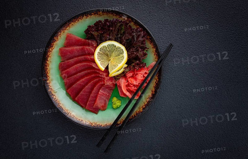 Fresh tuna sashimi served with lemon, wasabi, and pickled ginger on a dark background