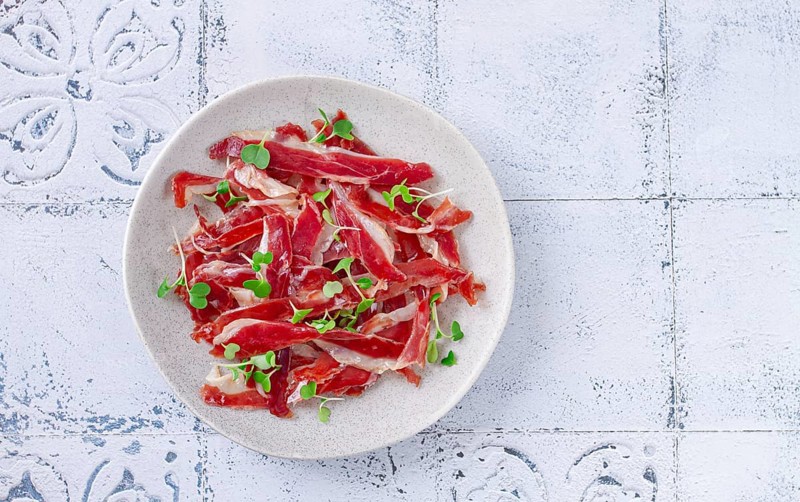 Ham of duck breast, dried duck fillet, with microgreens, plate, on a tiled table
