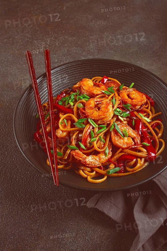Udon stir-fry shrimp noodles with red bell pepper and green onion, served in a black bowl, with chopsticks, dark background