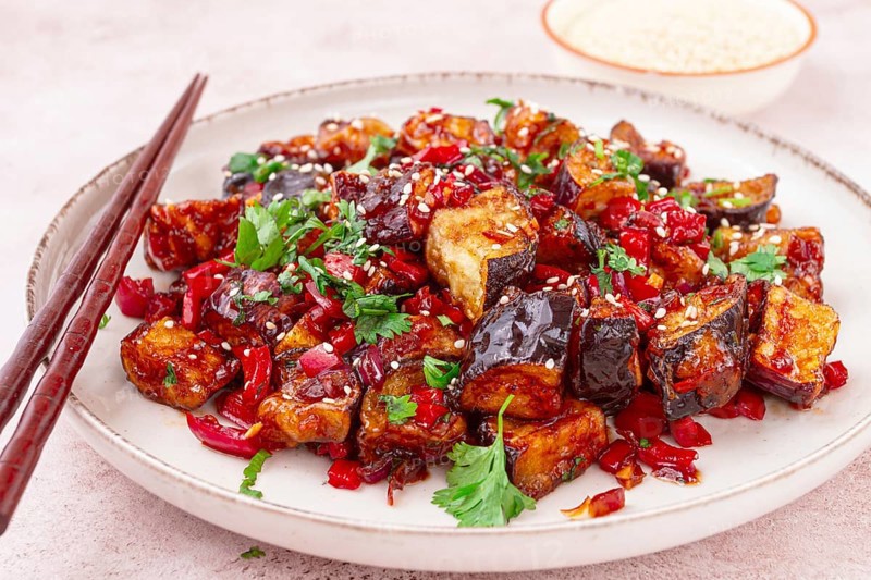 Fried eggplant, Chinese style, in sweet and sour sauce, with pepper and sesame seeds. on a white plate