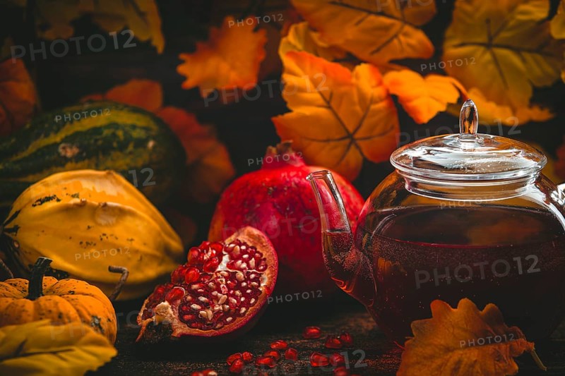 Teapot, pomegranate and pumpkins against a background of autumn leaves