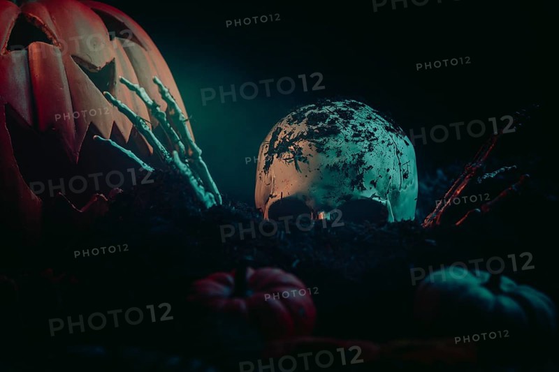 Halloween scene with a skull, skeletonised hands and pumpkins in dark earth