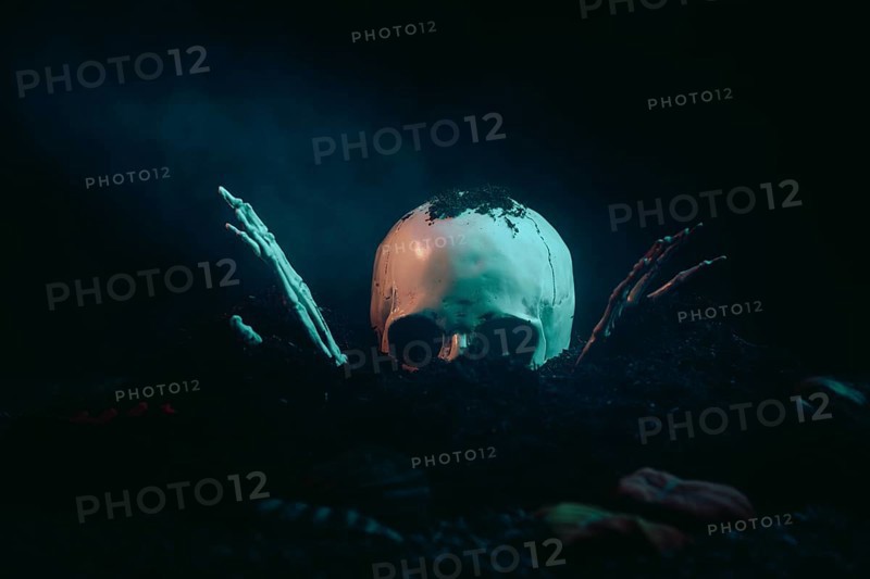 A skull with skeletonised hands bursts out of the earth in the moonlight, Halloween