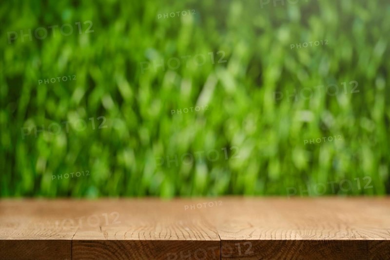 A simple wooden table stands in front of a softly blurred lush green grass background. The scene captures a sense of nature and tranquility. Ideal for outdoor dining or relaxation moments