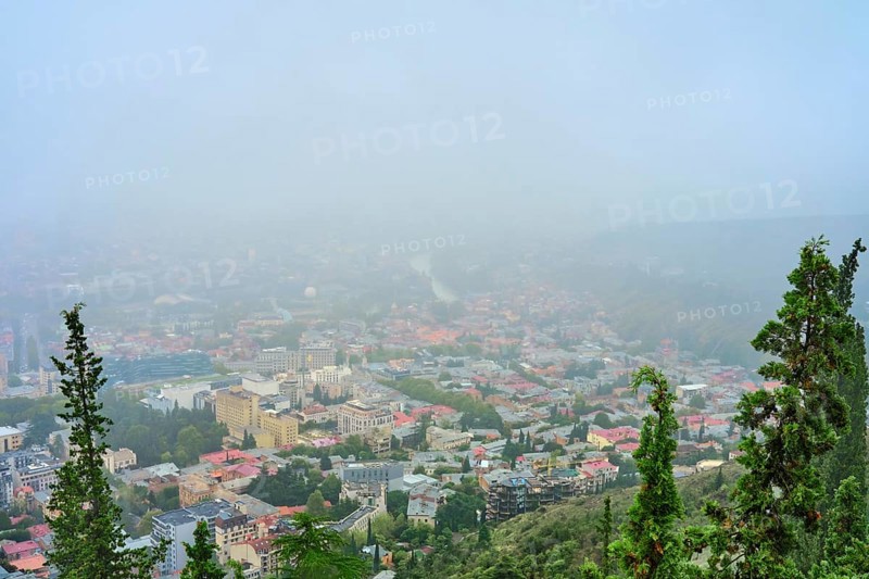 A dense fog blankets the city of Tbilisi, obscuring buildings and creating a mystical atmosphere