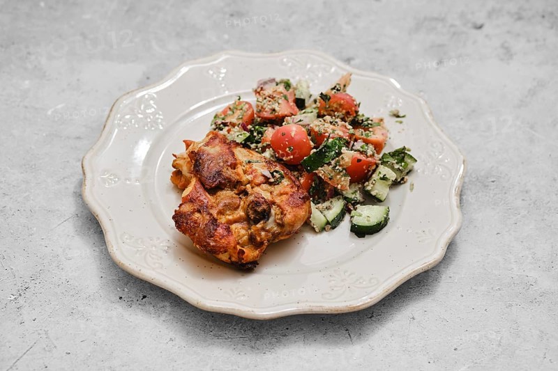 A hearty baked dish sits on a decorative plate alongside a vibrant vegetable salad. The salad features fresh tomatoes and cucumbers, creating a colorful and nutritious meal perfect for any time