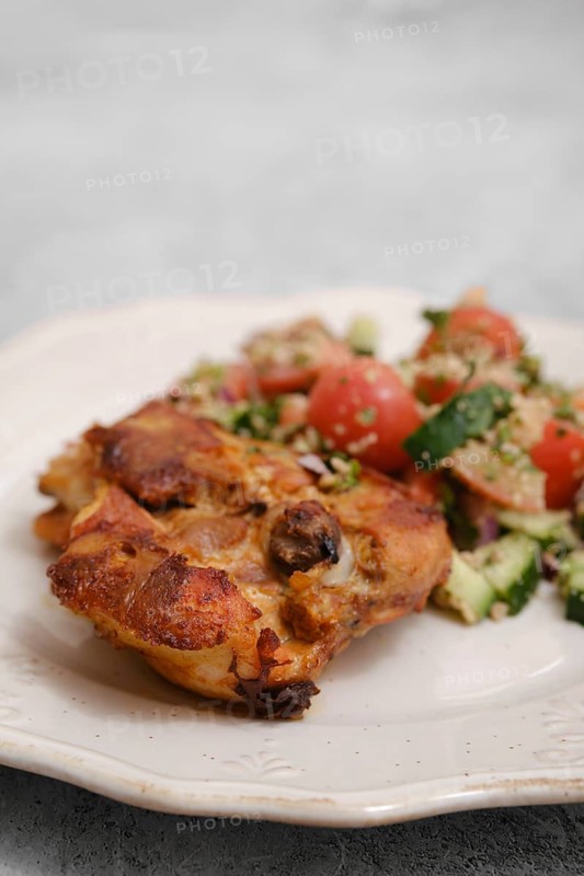 Juicy chicken piece rests on a plate beside a colorful salad made of tomatoes, cucumbers, and herbs. This meal showcases fresh ingredients perfect for a healthy lunch or dinner