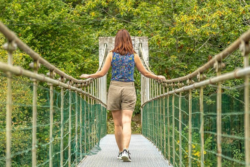 Female tourist enjoying a peaceful walk across a metallic hanging bridge, surrounded by lush green vegetation, on the route from the dobra river to the olla de san vicente in asturias, spain