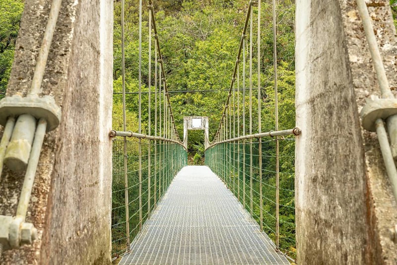 Metal suspension bridge crossing the sella river, connecting the dobra river route with the olla de san vicente, surrounded by lush vegetation in asturias, spain