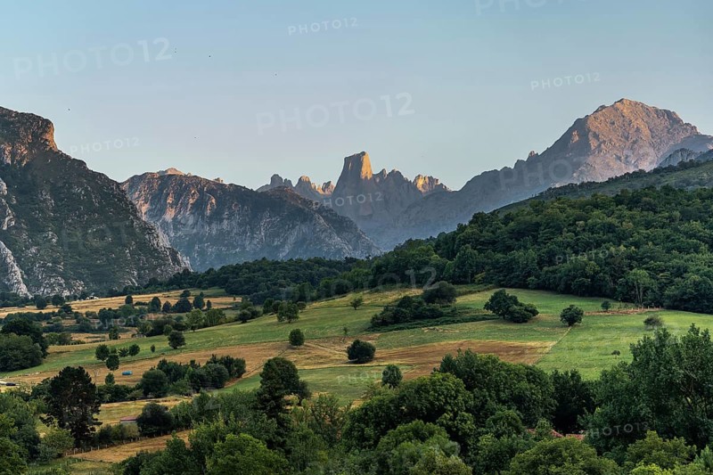 Golden hour sunlight illuminating the iconic naranjo de bulnes peak, towering over lush green valleys and forests in picos de europa national park, asturias, spain