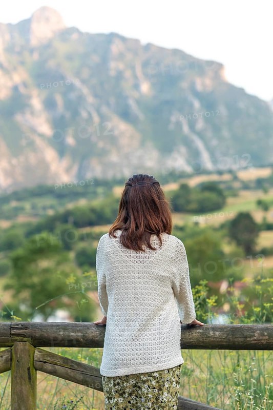 Woman leaning on a wooden fence, admiring the breathtaking view of picu urriellu, a stunning peak in picos de europa national park, asturias, spain