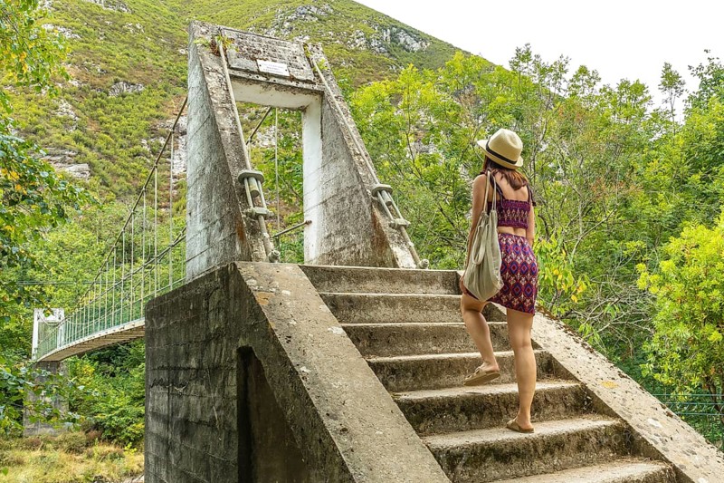 Female tourist walking up concrete stairs leading to an old suspension bridge over the dobra river in asturias, spain, enjoying the beautiful natural scenery and embarking on an adventurous journey