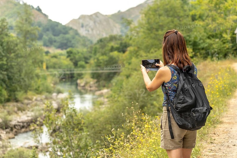 Female tourist with a backpack capturing photos of the dobra river along the scenic route to olla de san vicente in asturias, spain, on a sunny summer day