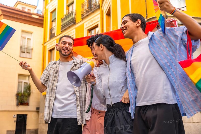 Group of happy young friends celebrating lgbtq plus pride, marching together in a city street with rainbow flags and a megaphone, sharing joy and community spirit