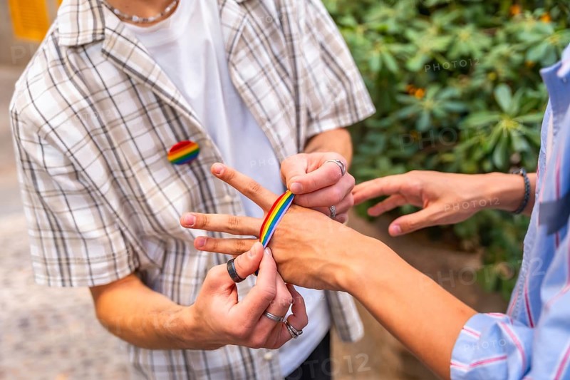 People are decorating their hands with rainbow colored adhesive tape, celebrating identity, community, and pride, with a rainbow pin visible on one person's shirt