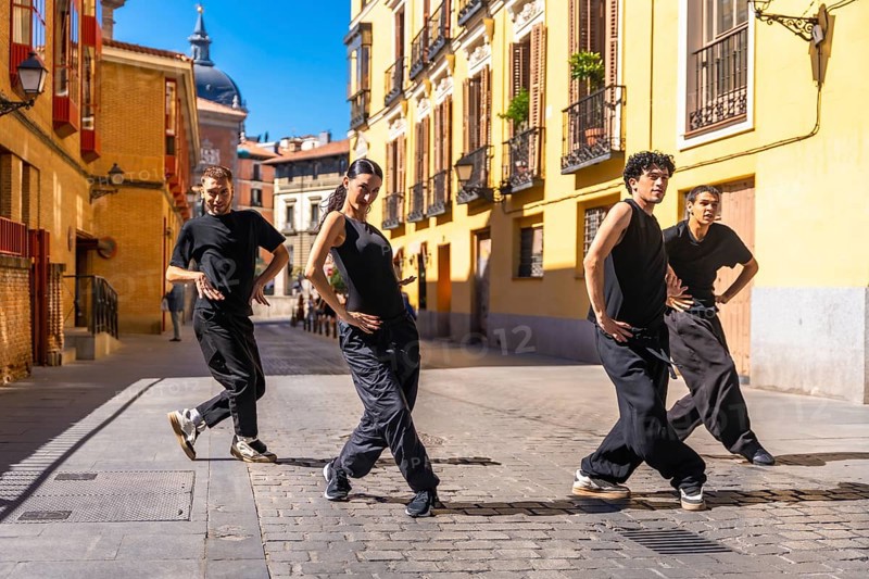 Group of urban dancers in black clothes performing a contemporary dance routine on a cobbled street in madrid, spain, showcasing artistic movement and urban culture