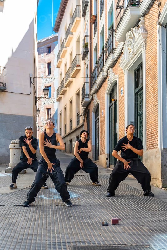 Group of four young dancers expressing movement and energy through a choreographed street performance in a narrow european alley, showcasing contemporary dance