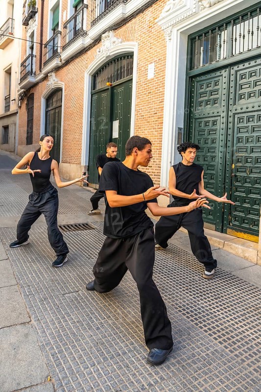 Group of young artists in black clothing performing a synchronized urban dance routine on a cobblestone street in a european city, expressing movement and creativity