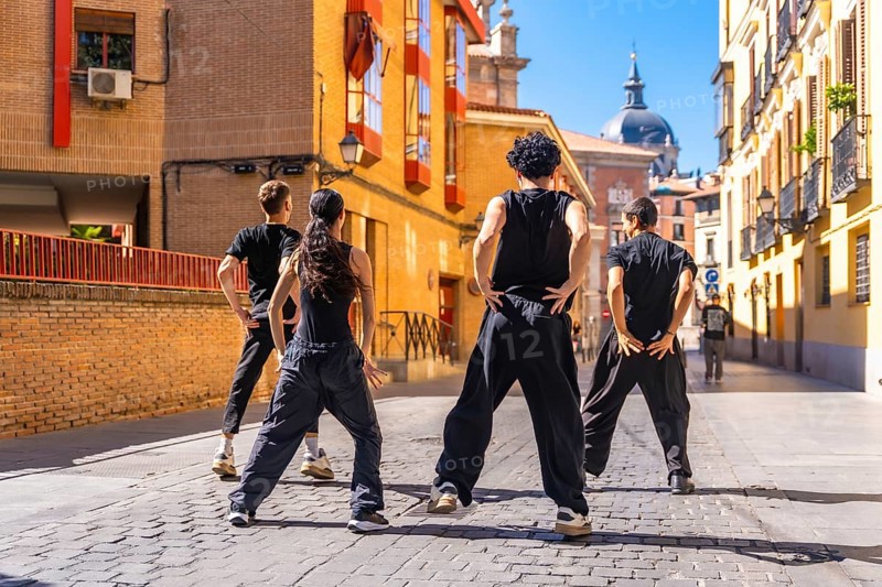 Group of young people standing in an urban cobblestone street, performing an energetic street dance routine together, showcasing teamwork and youthful expression
