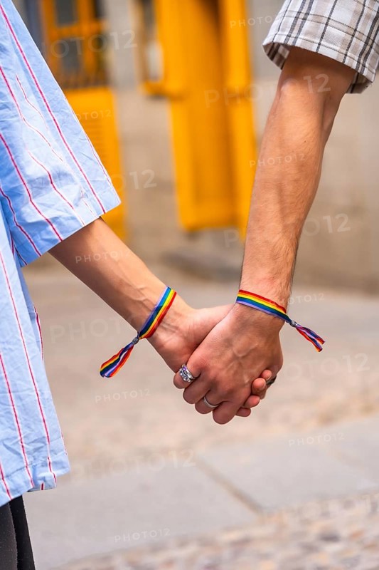 Couple's hands holding together, both wrists featuring rainbow bracelets, symbolizing love, pride, and support for the lgbtq plus community, representing equality