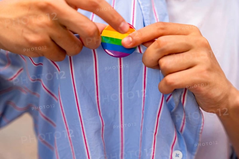 Person's hands carefully pinning a rainbow pride flag button onto a blue and white striped shirt, symbolizing support for lgbtq plus community, identity, and acceptance