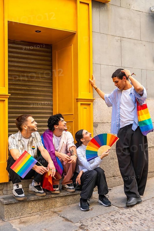 Group of four diverse friends celebrating lgbtq plus pride in the city, waving rainbow flags and a fan, smiling and showing unity, joy, acceptance and youthful solidarity