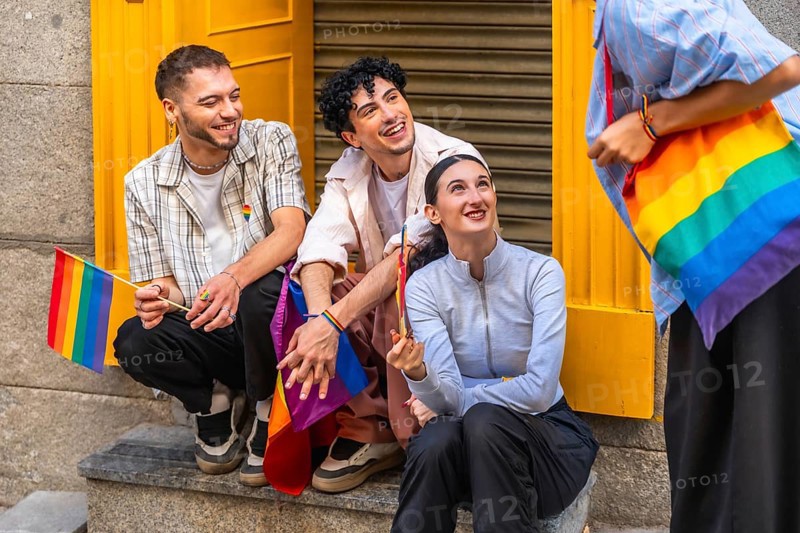 Group of diverse friends expressing joy and belonging, holding rainbow flags and carrying a rainbow bag, celebrating gay pride and lgbtqia plus inclusion in a city environment