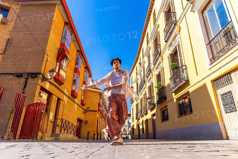 Young man freely dancing in a cobblestone street between traditional architecture buildings under a bright blue sky, moving with joy and expressing freedom