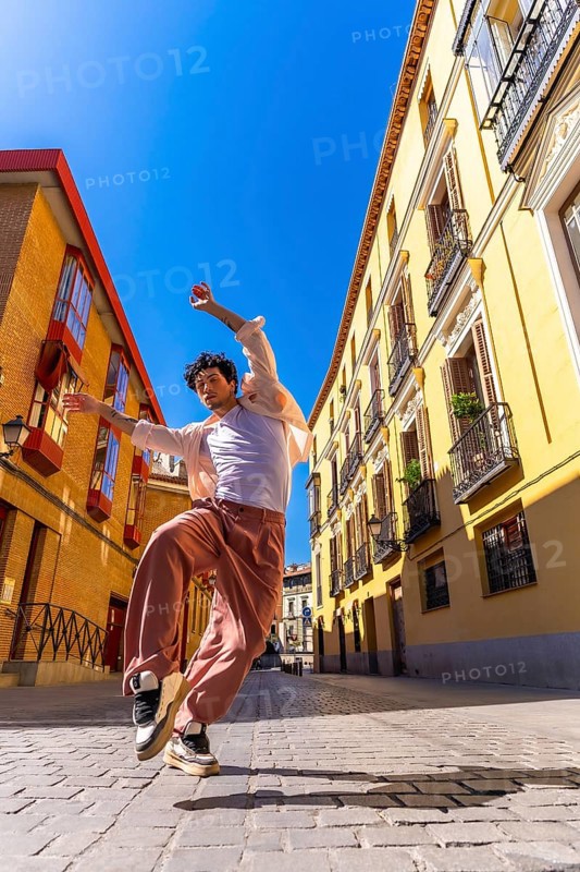 Man dancing energetically on a sunny cobblestone street in madrid, showcasing urban style and contemporary movement, freedom, joy and confident street performance